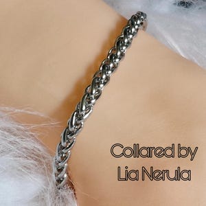 May include: A silver braided chain bracelet. The bracelet is on a person's wrist. The text "Collared by Lia Nerula" is visible in the image.