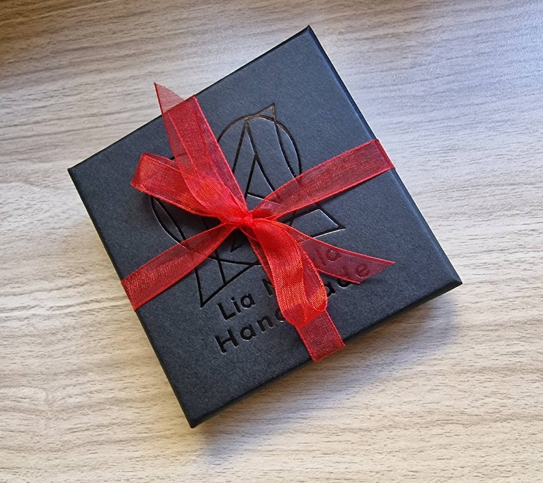May include: A black gift box with a red ribbon tied around it. The box has the text "Lia Made Handmade" printed on it.