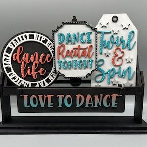 May include: Three wooden signs with dance-themed text on a black stand. The signs read "Dance Life", "Dance Recital Tonight", and "Twirl & Spin". The stand has the words "Love to Dance" written on it.