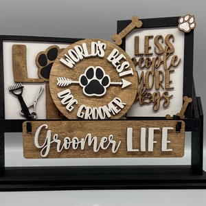 May include: A wooden dog groomer sign with a black base and frame. The sign features the words "LOVE", "WORLD'S BEST DOG GROOMER", and "LESS people MORE dogs". Decorative elements include paw prints, a bone, and grooming tools.