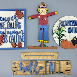 May include: A set of four wooden signs with a fall theme. The signs feature the text "leaves are falling autumn is calling", "hello fall", and "scarecrow on duty". The set also includes a wooden scarecrow figure.