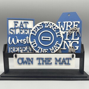 May include: A white ceramic mug with a black handle and the text "But First, Coffee" in a bold, black font. The mug is filled with a dark liquid, likely coffee, and sits on a light-colored surface.