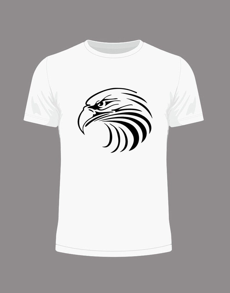 May include: White t-shirt featuring a black graphic of an eagle's head in profile. The eagle design is detailed with sharp lines, emphasizing the bird's beak and eye. The shirt has a classic crew neck and short sleeves.