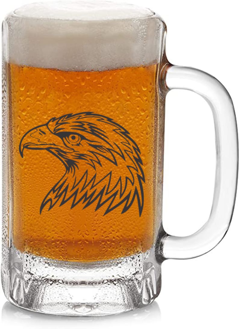 May include: A clear glass beer mug filled with amber-colored beer and a foamy white head. A black graphic of an eagle's head is on the front of the mug. The mug has a handle and is covered in condensation.