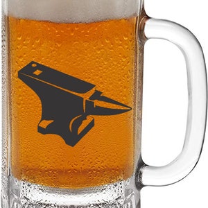 May include: A clear glass beer mug with a handle, filled with a light amber colored beer. The mug has a black silhouette of an anvil printed on the front.