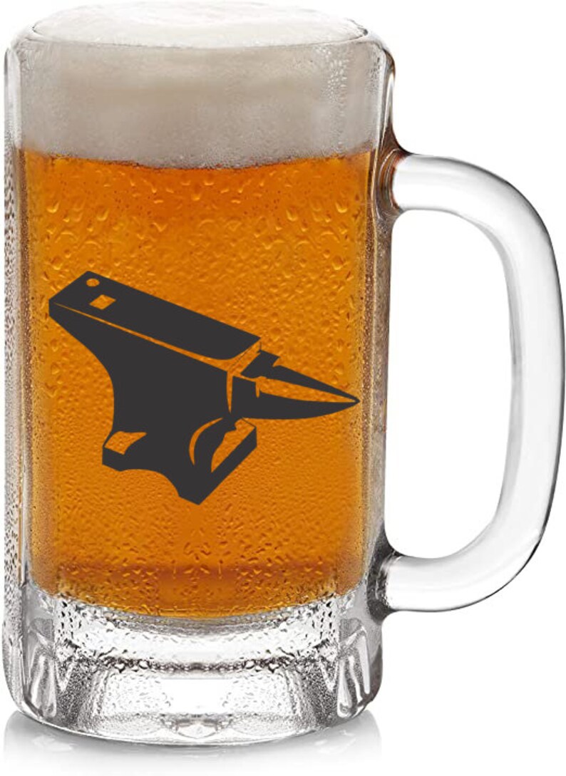 May include: A clear glass beer mug with a handle, filled with a light amber colored beer. The mug has a black silhouette of an anvil printed on the front.