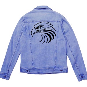 May include: Light blue denim jacket with a black eagle head design on the back. The jacket has a classic button-up design with two chest pockets and two side pockets. The eagle graphic is a stylized, tribal-inspired design.