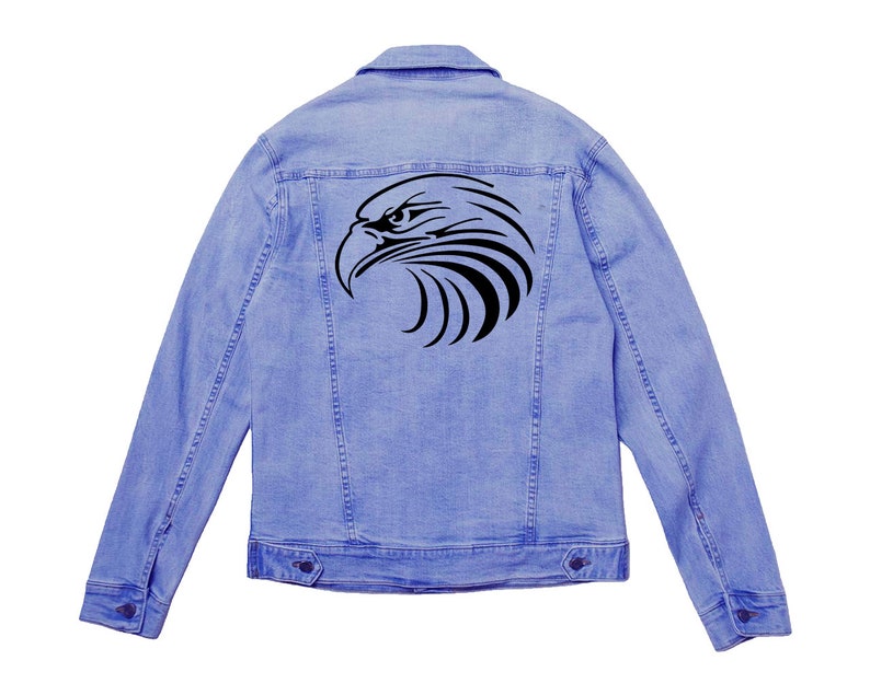 May include: Light blue denim jacket with a black eagle head design on the back. The jacket has a classic button-up design with two chest pockets and two side pockets. The eagle graphic is a stylized, tribal-inspired design.
