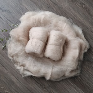 Könnte beinhalten: Zwei beige, flauschige, zusammengerollte Stoffstücke, die mit Schnur gebunden sind, liegen in einem größeren, beige, flauschigen Stoffstück.