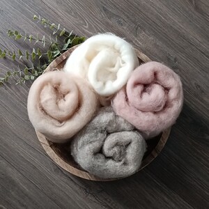 May include: Four rolled up fabric swatches in a wooden bowl. The swatches are in shades of beige, light brown, gray, and pink.