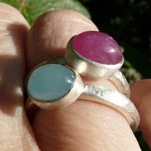May include: Two silver rings with oval-shaped gemstones. The top ring has a pink gemstone and the bottom ring has a light blue gemstone.