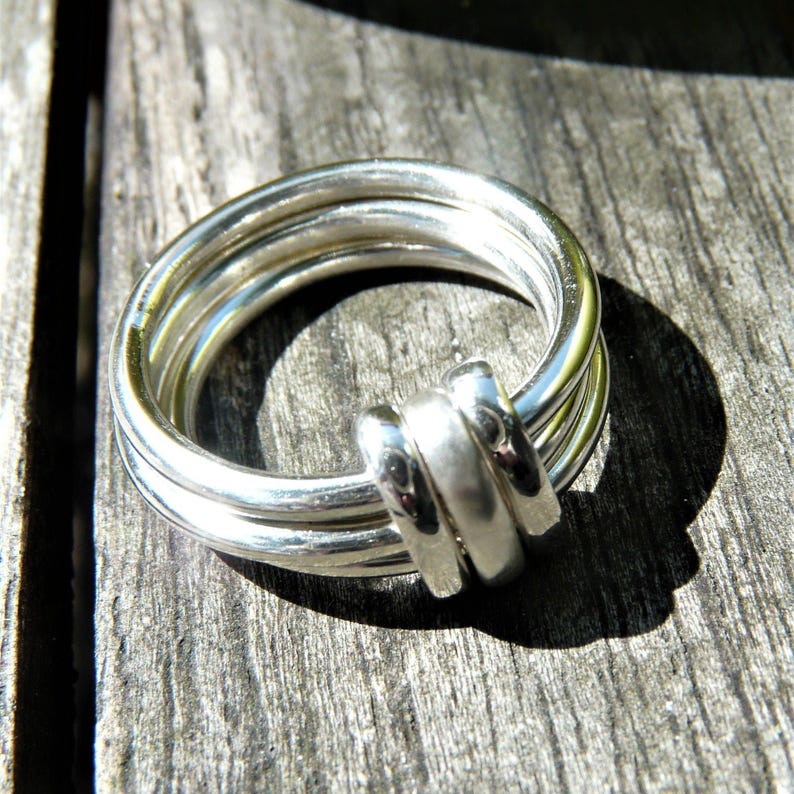 Hand made 2mm sterling silver wire kinetic fidget ring set with your choice of charms. The picture shows 3 silver charms connecting all 3 rings together, but others are available including 9ct solid gold, patinated blackened silver as well as extra charms. The 3 solid silver or red gold charms gently and easily move round the 3 silver bands and are lovely to fiddle with.
The rings are all hand made by me using recycled and eco friendly sterling silver and hallmarked red gold wire.