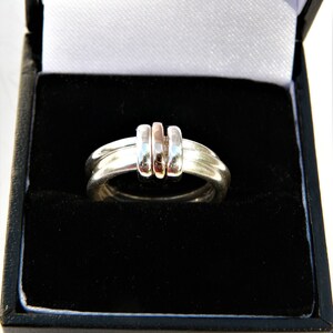 May include: A silver ring with three bands, two are silver and one is rose gold. The ring is in a black velvet ring box.
