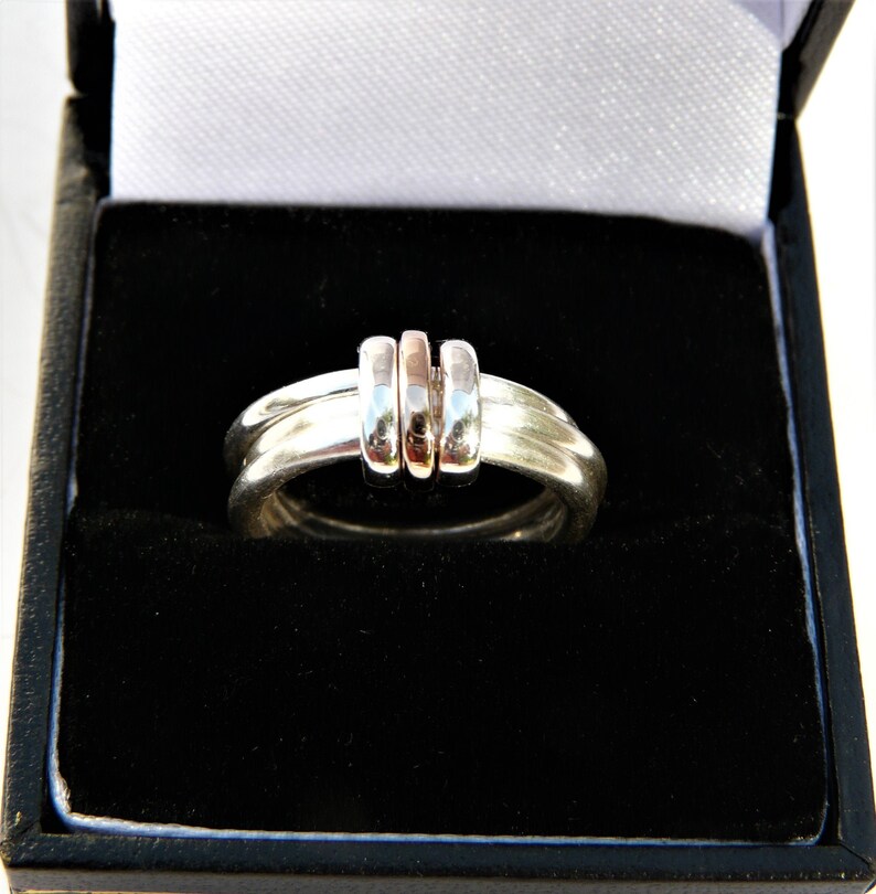 May include: A silver ring with three bands, two are silver and one is rose gold. The ring is in a black velvet ring box.