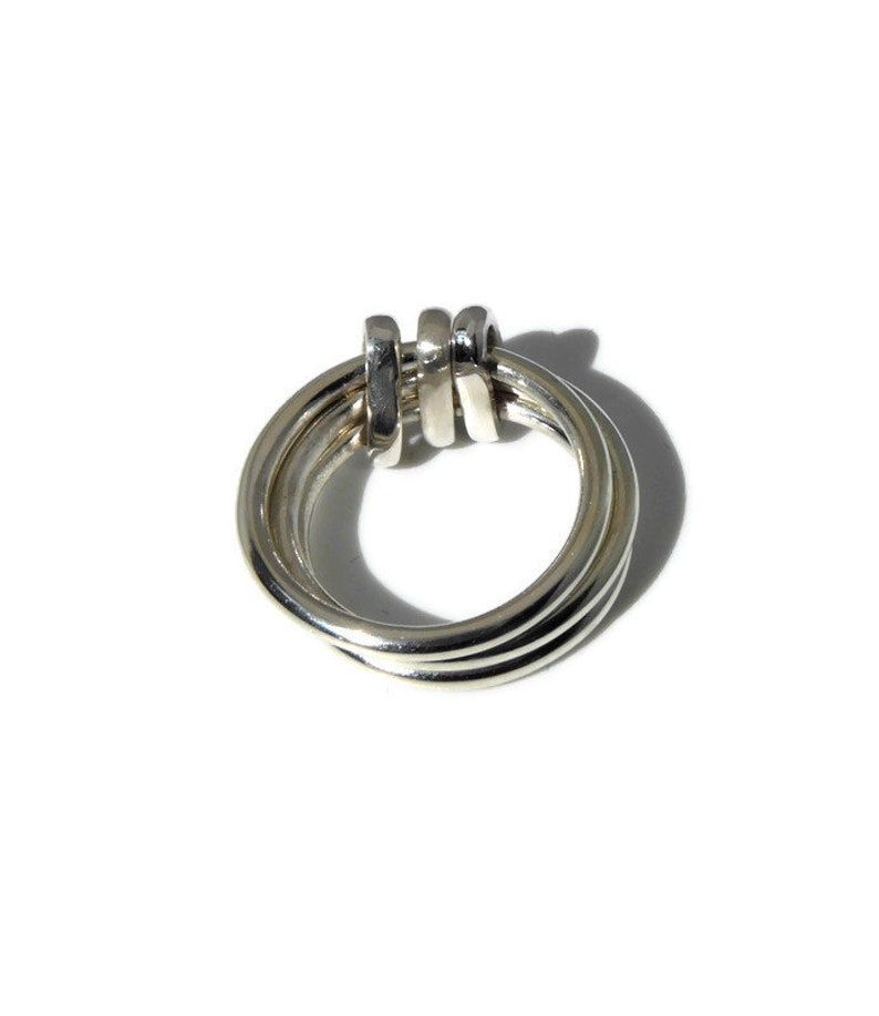 May include: A silver ring with three interlocking bands.