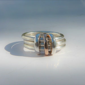 May include: A silver ring with three bands and a rose gold accent in the center.