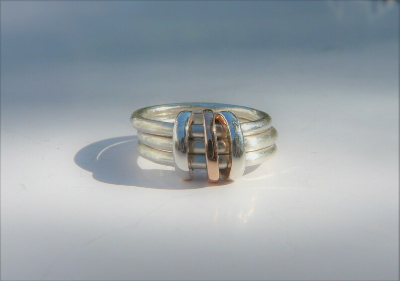 May include: A silver ring with three bands and a rose gold accent in the center.