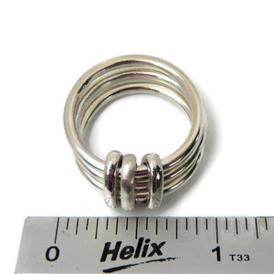 May include: A silver ring with four bands that are twisted together at the top. The ring is measured against a ruler that reads "Helix" and has markings in inches.