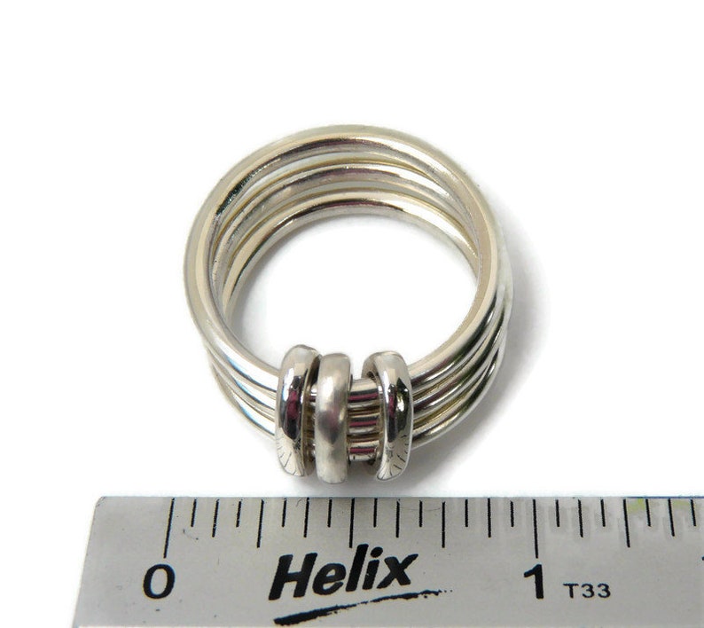 May include: A silver ring with four bands that are twisted together at the top. The ring is measured against a ruler that reads "Helix" and has markings in inches.