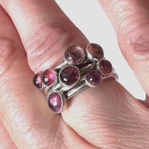 May include: A set of four silver rings with pink gemstones. Each ring features a single round gemstone, and the rings are stacked on top of each other.