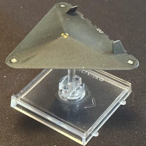 May include: A black triangular model airplane on a clear plastic stand. The model has a flat top and a pointed nose. The model is on a clear plastic stand with a black base.