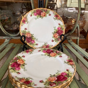May include: A set of four white porcelain teacups and saucers with a gold rim and a floral pattern featuring red, yellow, and pink roses.