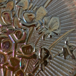 Peut inclure: Gros plan d'un plat en verre iridescent vintage avec un motif floral. Le plat a une surface textur&eacute;e avec un motif de lignes diagonales. Les fleurs sont dans des tons de brun, rose et violet.