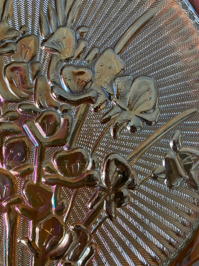 Peut inclure: Gros plan d'un plat en verre iridescent vintage avec un motif floral. Le plat a une surface textur&eacute;e avec un motif de lignes diagonales. Les fleurs sont dans des tons de brun, rose et violet.