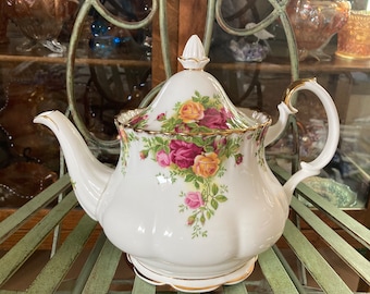May include: A white porcelain teapot with a floral pattern of roses and green leaves. The teapot has a gold trim and a lid with a knob.
