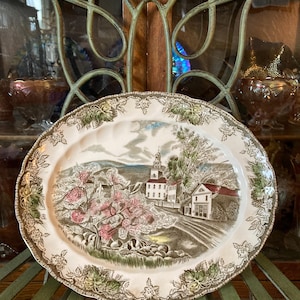 May include: A vintage oval ceramic serving platter with a brown, green and white floral pattern. The centre of the platter features a detailed illustration of a small town with a church, houses and trees.