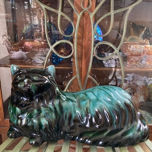 May include: A ceramic cat figurine in a reclining pose. The cat is glazed in a dark green and black colour scheme with a glossy finish.