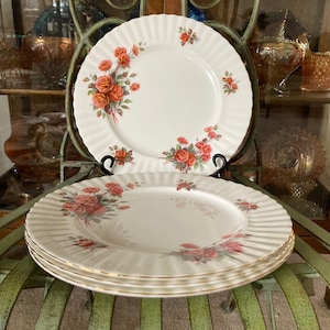 May include: Three white dinner plates with a gold rim and a floral pattern of pink and orange roses. The plates are stacked on top of each other.