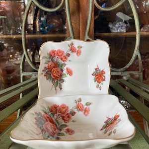 May include: Two white porcelain square-shaped dishes with a gold rim and a floral design featuring pink and red roses. The dishes are stacked on top of each other.