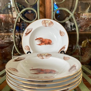 Peut inclure: Ensemble de quatre bols à soupe blancs avec un bord doré. Chaque bol présente un motif peint à la main d'un homard et de coquillages.