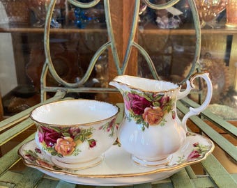 Peut inclure: Un service à thé en porcelaine blanche avec un motif floral. L'ensemble comprend un pot à crème, un sucrier et un plateau. Le motif floral présente des roses rouges, jaunes et roses.