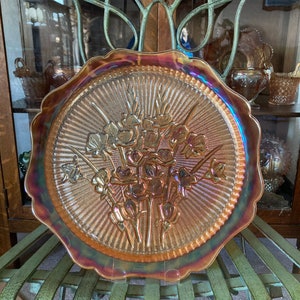 Peut inclure: Une grande assiette de service en verre ambr&eacute; iridescent avec un motif floral en relief. L'assiette a un bord festonn&eacute; et une surface textur&eacute;e.