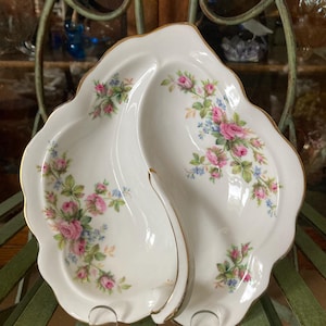 Peut inclure: Un plat de service en porcelaine blanche avec un bord doré et un motif floral. Le plat est divisé en deux sections, chacune avec un bord festonné.