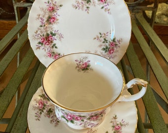 May include: A white teacup and saucer set with a floral pattern of pink roses and green leaves. The set has a gold trim around the edges.