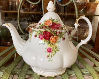 May include: A white porcelain teapot with a floral pattern featuring red, yellow, and pink roses. The teapot has a gold trim and a lid with a finial.