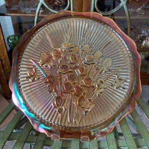 Peut inclure: Une grande assiette en verre ambr&eacute; iridescent avec un bord festonn&eacute;. L'assiette pr&eacute;sente un motif en relief d'un bouquet de fleurs.