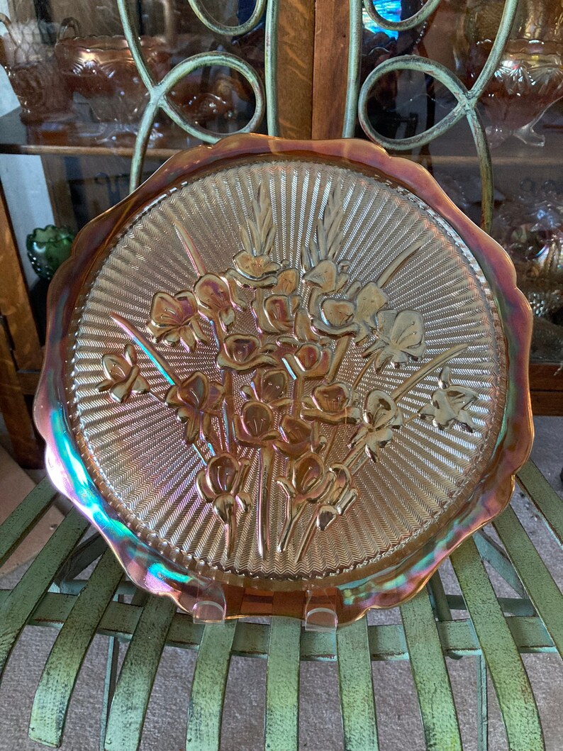 Peut inclure: Une grande assiette en verre ambr&eacute; iridescent avec un bord festonn&eacute;. L'assiette pr&eacute;sente un motif en relief d'un bouquet de fleurs.