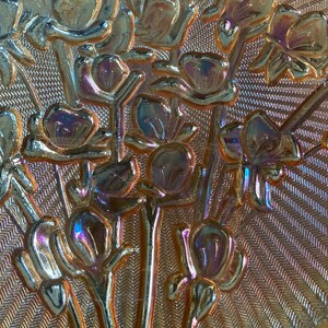 Peut inclure: Gros plan d'un plat en verre iridescent vintage avec un motif floral. Le plat a une surface textur&eacute;e et un bord festonn&eacute;.