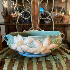 May include: A blue and white ceramic planter with a floral design. The planter has two handles and features a raised design of white flowers with yellow centres.