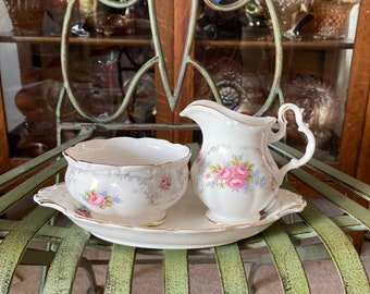 May include: A white porcelain sugar bowl and creamer set with a floral design. The set is on a green metal tray.