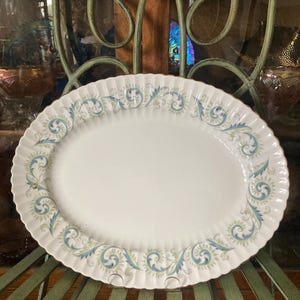 May include: A white oval serving platter with a blue and green floral pattern around the edge. The platter has a gold rim.