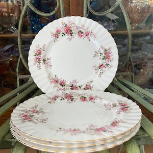 May include: Three white ceramic dinner plates with a gold rim and a floral pattern of pink roses and green leaves.
