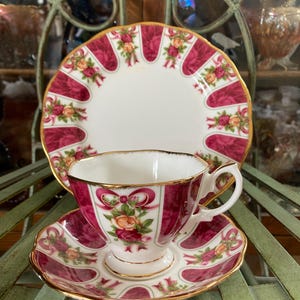 May include: A vintage teacup and saucer set with a pink and gold floral pattern. The cup and saucer feature a delicate floral design with bows and ribbons.