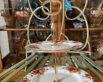 Peut inclure: Un support à gâteau à deux étages avec une base en métal doré et deux assiettes en porcelaine blanche à motif floral. Les assiettes présentent un motif floral rouge, jaune et rose avec des accents dorés.