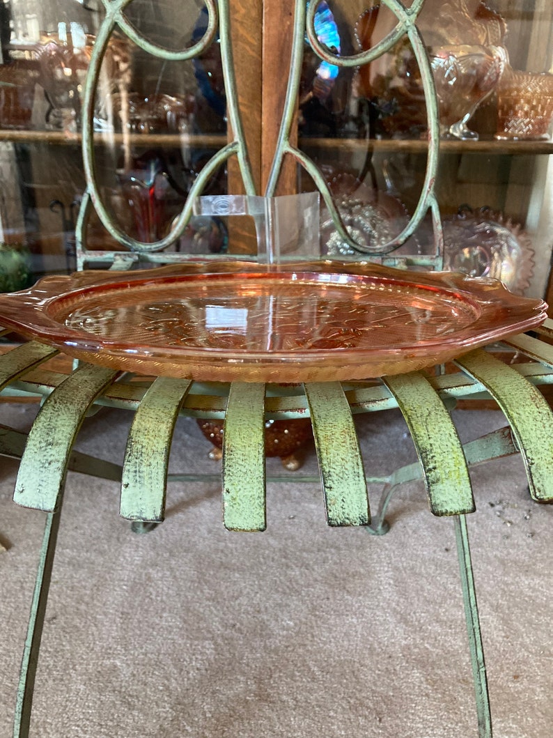 Peut inclure: Un plateau de service en verre vintage de couleur p&ecirc;che avec un motif d&eacute;coratif. Le plateau est pos&eacute; sur une chaise en m&eacute;tal vert.