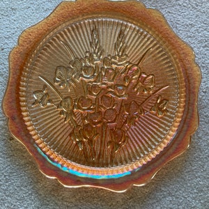 Peut inclure: Une assiette en verre ambr&eacute; vintage avec un bord festonn&eacute; et un motif floral. L'assiette a une surface textur&eacute;e et une finition iris&eacute;e.